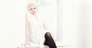 Hilde Louise Asbjørnsen i hvit kjole sittende i et vindu